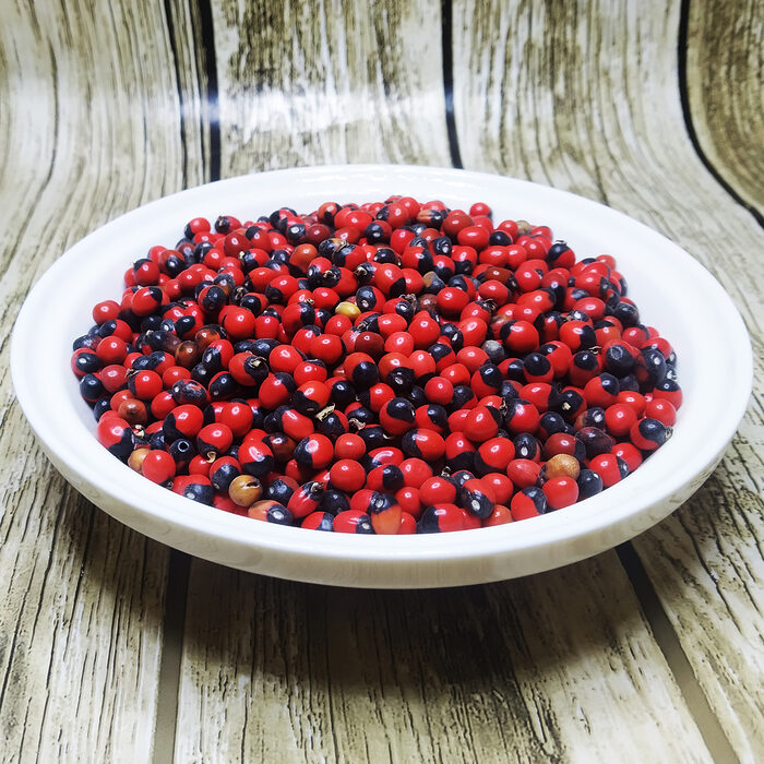 A pile of vivid red and black Abrus Precatorius seeds known as Chirmi Ratti Gunja lucky beads scattered on a white background showing their characteristic two-toned glossy surface - Variation