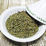 Close-up of dried green Moroccan juniperus needle leaves piled in a white ceramic bowl on a rustic wooden surface - Variation