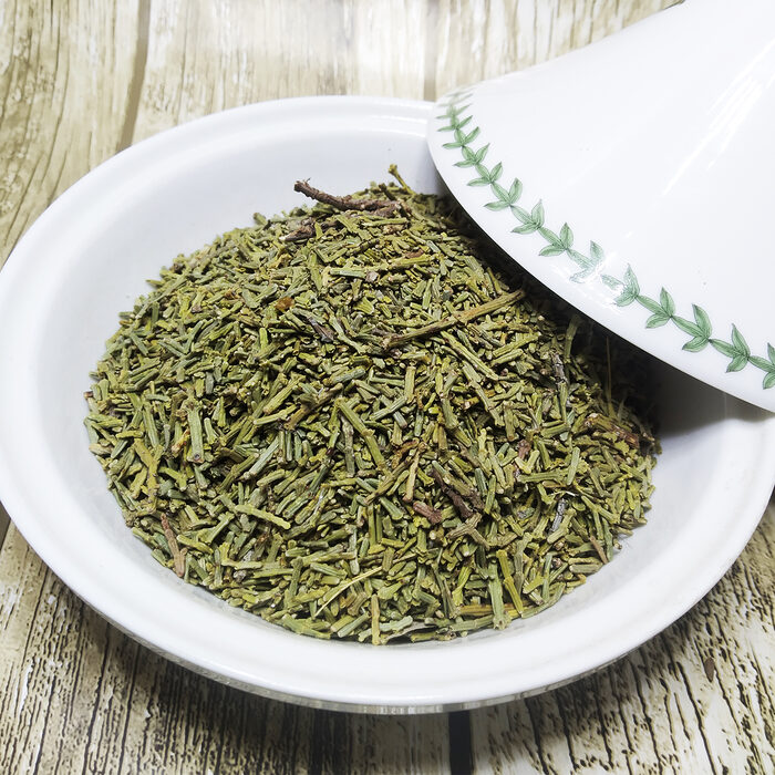 Close-up of dried green Moroccan juniperus needle leaves piled in a white ceramic bowl on a rustic wooden surface - Variation