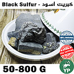 Raw dark grey-black sulfur mineral chunks displayed in a white Moroccan ceramic tagine bowl on a wooden surface, showing natural unprocessed texture with yellow sulfur veins