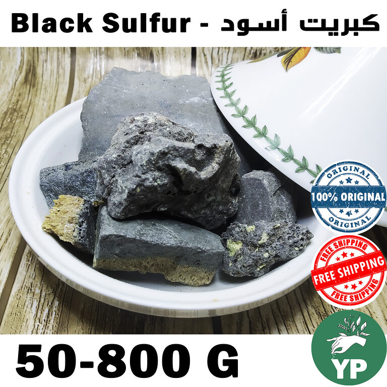 Raw dark grey-black sulfur mineral chunks displayed in a white Moroccan ceramic tagine bowl on a wooden surface, showing natural unprocessed texture with yellow sulfur veins