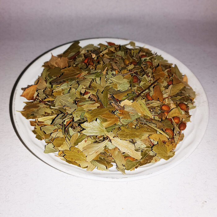 Dried hawthorn leaves in shades of green and golden-brown displayed on a white round plate against a light background - Variation