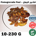 Dried dark brown pomegranate peel pieces arranged on a white ceramic plate, showing natural texture and color variation from deep brown to golden yellow
