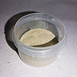 Fine beige-gold palm pollen powder in a transparent plastic container, viewed from above on a light textured background - Variation