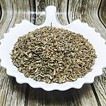 Dried wild carrot seeds piled in a white scalloped ceramic dish on a dark marble surface, showing small olive-green ridged seeds - Variation