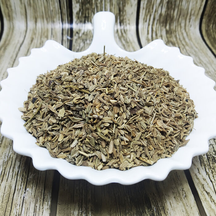 Dried wild carrot seeds piled in a white scalloped ceramic dish on a dark marble surface, showing small olive-green ridged seeds - Variation